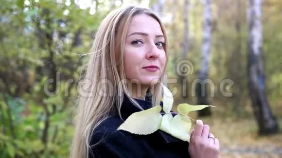 美丽的年轻女子的肖像把秋天的树叶放在森林里4K慢动作3840x2160视频的预览图