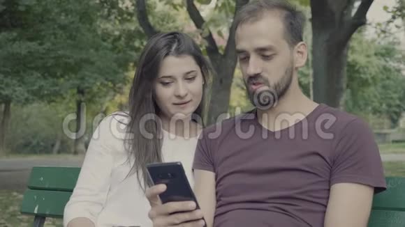 公园里坐在长椅上看智能手机的情侣视频的预览图