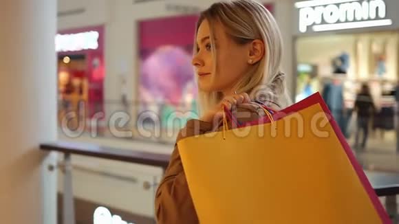 年轻女孩在她的手机里输入一些东西带着购物袋在商场里走来走去视频的预览图