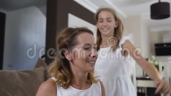 在客厅里一位身穿白色长裙的快乐少女正在拥抱美丽的妈妈并大笑视频的预览图