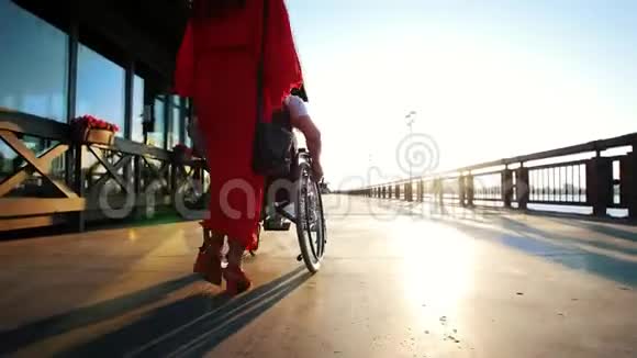 穿橙色衣服的女孩在阳光下的海滨坐轮椅的男人视频的预览图