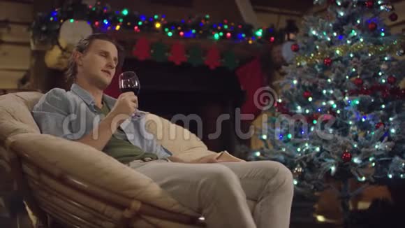 长头发的男人在圣诞夜用装饰好的树喝酒视频的预览图