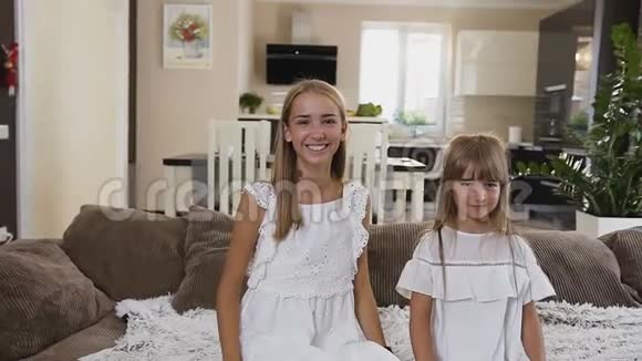 在酒店房间里两个快乐的十几岁的姐妹躺在床上的慢镜头穿着白色裙子的漂亮快乐的女孩视频的预览图