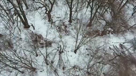 冬季寒冷的一天穿黄色外套的慢跑者在森林中奔跑的空中射击视频的预览图