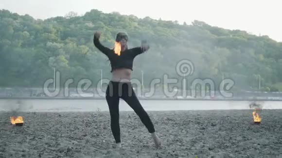 自信苗条的女人戴着面具跳舞表演一场站在河岸上的火球表演熟练的射击技巧视频的预览图