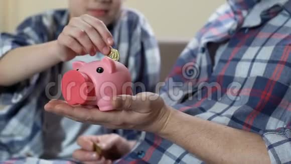 儿子和父亲把硬币放在储蓄罐里快乐地拥抱着读金融知识视频的预览图