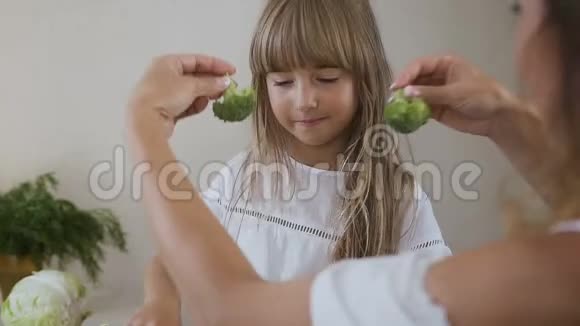 一个小女孩的两个女人和她的妈妈正在玩用新鲜的西兰花做耳环很漂亮的女孩视频的预览图