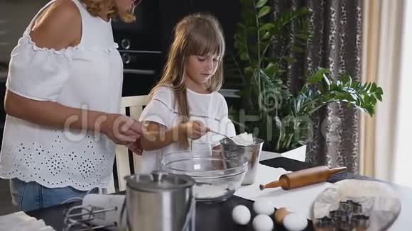 漂亮的年轻母亲准备做饭的一切把面粉倒在玻璃碗里女儿帮忙视频的预览图