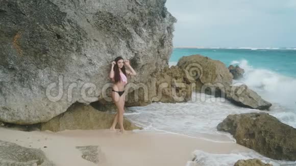 慢镜头穿着泳装在沙滩上摆姿势的美丽性感女孩的肖像背景是波浪拍摄的是Stealam视频的预览图