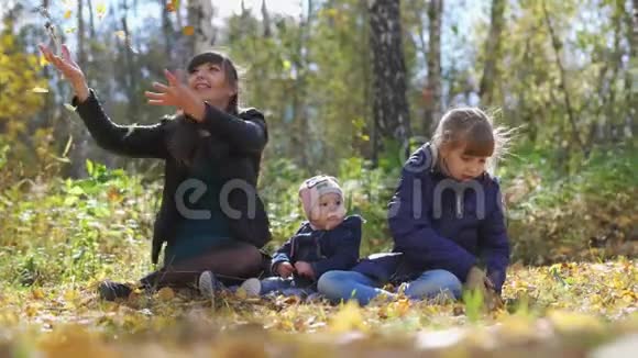 在一个阳光明媚的秋日带着孩子扔树叶的年轻妈妈一家在公园里放松慢动作3840x21604K视频的预览图