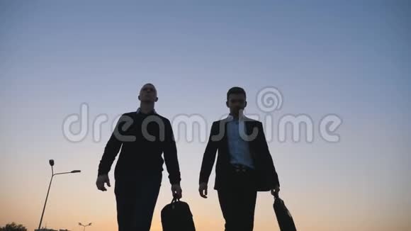 两位年轻的成功商人在晚上下班后穿着公文包走路时的低角度视角视频的预览图