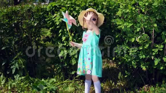 夏天小女孩在绿色灌木丛的背景上拿着风车视频的预览图