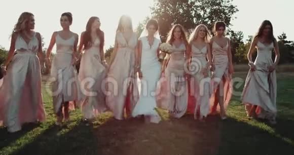 伴娘和新娘美丽地走在草地上有着惊人的日落背景红色史诗4k视频的预览图