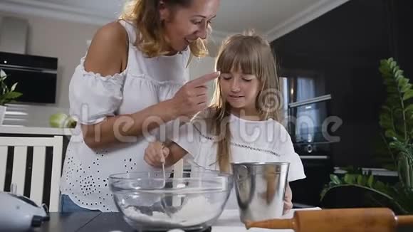 特写镜头幸福的年轻家庭在厨房做饭妈妈和她的小女儿正在准备一个面团来烘烤视频的预览图