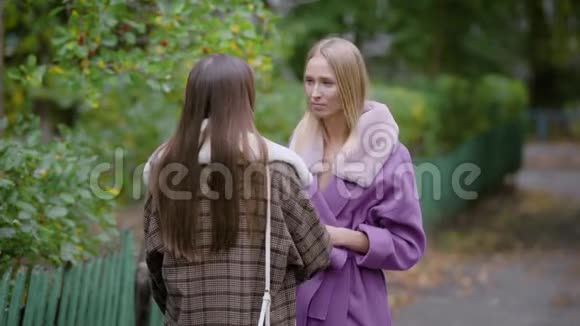 在秋天的公园里一位金发的年轻女子和她的黑发朋友在街上聊天视频的预览图