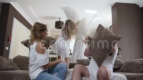 微笑的年轻家庭在客厅打枕头仗高加索快乐的母亲父亲和他们的两个孩子视频的预览图