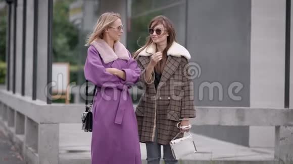 两个穿着外套的时髦女人站在城市街道上互相交谈视频的预览图