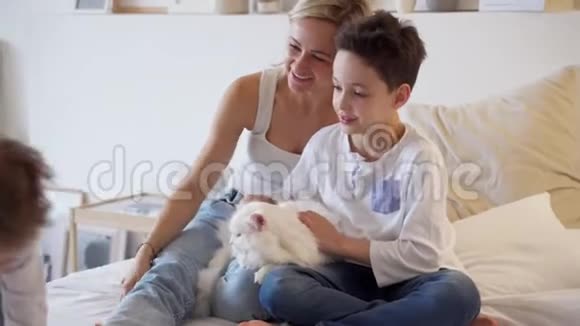 快乐的周末年轻的妈妈和快乐的孩子在床上玩耍姜白猫躺在床上躺在真正的室内视频的预览图