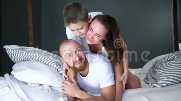 幸福的一家人穿着白色T恤衫躺在床上在家里的房间里视频的预览图