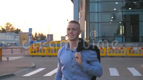 年轻的商人肩上扛着一件夹克在办公楼的背景下走在城市街道上快乐视频的预览图