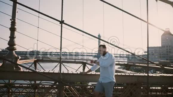 快乐的白种人独自站在布鲁克林大桥上在阳光明媚的夏日里一边看一边使用智能手表手镯视频的预览图