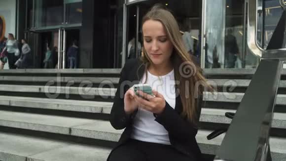商务女性坐在城市建筑的台阶上使用智能手机视频的预览图