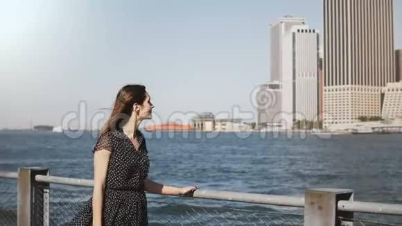 美丽的笑容可掬的白种人女人头发飞扬走在著名的纽约市金融中心的河畔天际线上视频的预览图