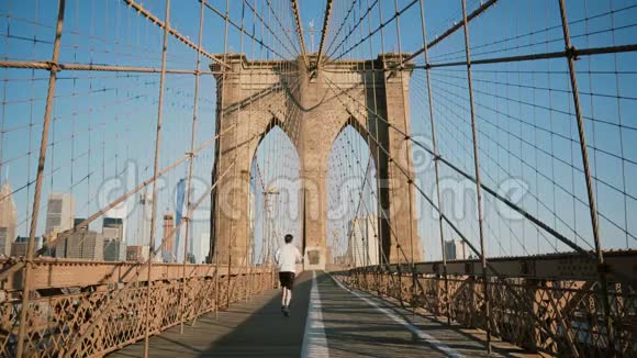 在阳光明媚的夏日男运动员沿着纽约布鲁克林大桥跑步美丽建筑低角度拍摄4K视频的预览图