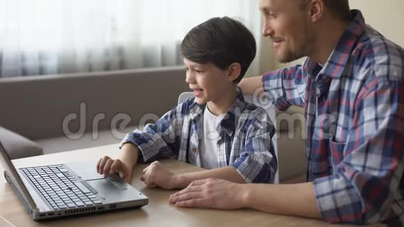 快乐的父亲教他的儿子在家里用笔记本电脑工作家庭护理视频的预览图