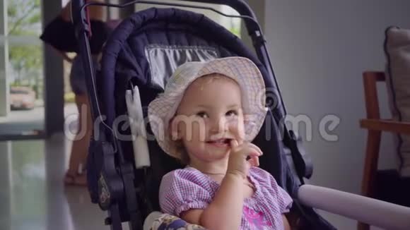 戴帽子的小女孩坐在蓝色的婴儿车里用手舔嘴动作缓慢视频的预览图