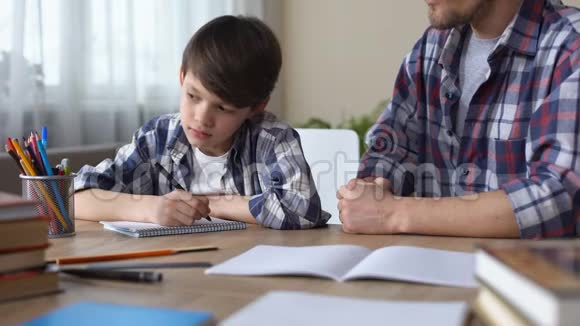 无聊的小男孩和严厉的父亲一起做作业悲伤的孩子望着窗户视频的预览图