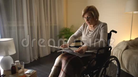 老妇人坐在轮椅上在家看报纸健康问题视频的预览图