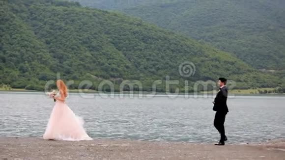 新娘和新郎在大河和风景如画的山脉附近浪漫地散步结婚纪念日视频的预览图