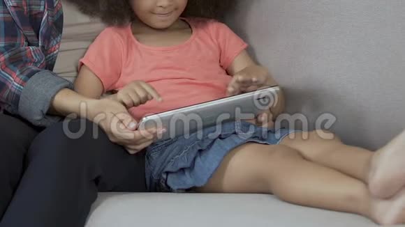 可爱的卷发女孩在平板电脑家里玩游戏和妈妈一起玩做父母视频的预览图
