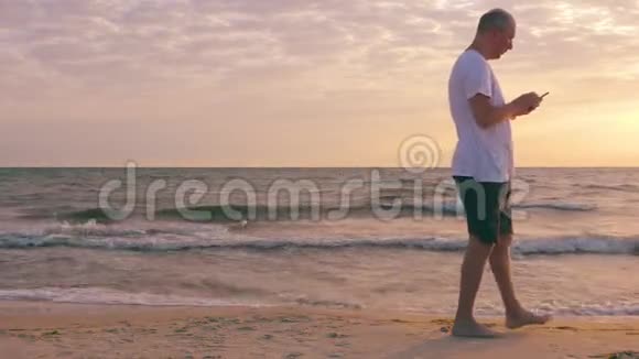 早上在海边散步时使用手机的成年男子视频的预览图