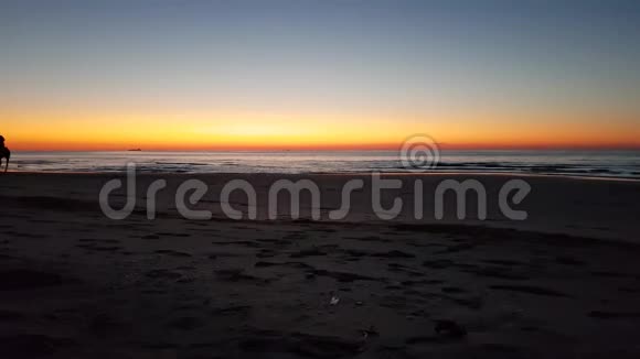 在橙色的天空背景下在沙滩上骑马的人视频的预览图