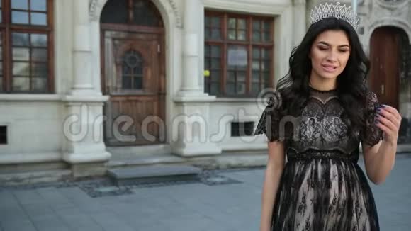 美丽的女孩黑发身穿黑色连衣裙头上戴皇冠摆姿势拍照视频的预览图