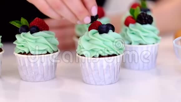甜点厨师女性手工装饰美味的纸杯蛋糕绿松石奶油与覆盆子和蓝莓在厨房视频的预览图