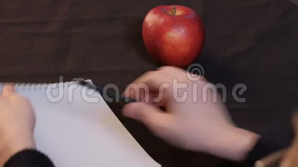 一个红苹果躺在黑色桌布上少年特写的手在桌上放下笔记本和笔视频的预览图