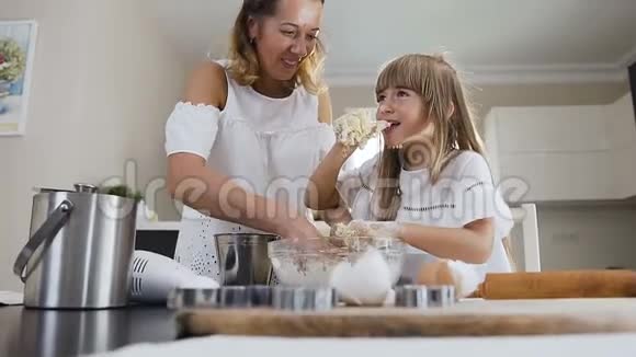 这位可爱的小女孩和她年轻的母亲的特写手里拿着面团因为他们揉捏它并品尝它快乐视频的预览图