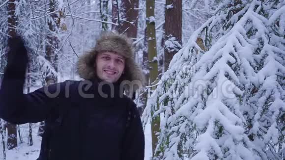 快乐的人走在寒冷的冬天的森林里向相机挥手覆盖着雪视频的预览图
