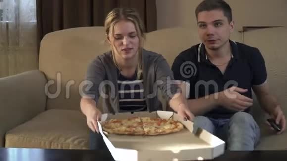 年轻夫妇带着一盒披萨坐在沙发上视频的预览图