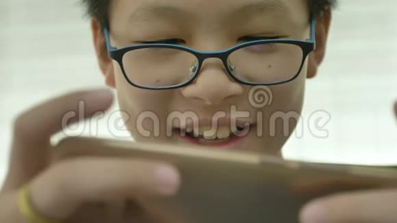 关闭年轻的亚洲男孩在智能手机上玩游戏与反射蓝盒眼镜视频的预览图
