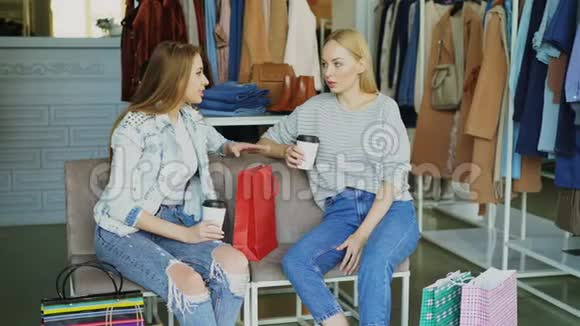 两个年轻的女人坐在皮革覆盖的椅子上穿着服装精品店购物后聊天漂亮的现代女人视频的预览图