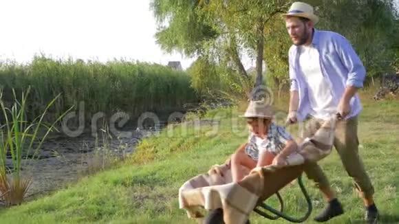 家庭户外度假快乐的爸爸带着快乐的孩子在手推车上慢动作着大自然视频的预览图