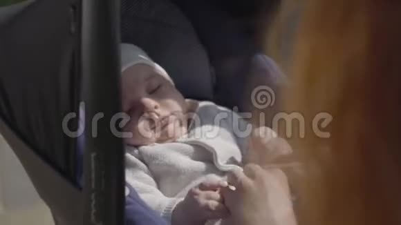 在公园的特写镜头中一位美丽的红发女子和她的婴儿躺在婴儿车里玩耍女士视频的预览图