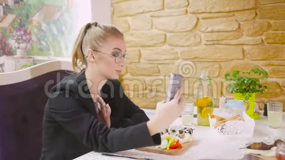 一个年轻女孩坐在餐厅的桌子旁在智能手机上自拍视频的预览图