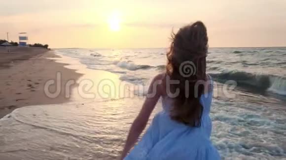 日落时女孩在浅水中奔跑一个穿着白色裙子的女孩正在水的边缘附近奔跑视频的预览图