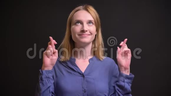 有吸引力的白种人金发女人的肖像用手势示意交叉手指以显示黑色背景上的希望视频的预览图