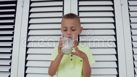 年轻的白种人男孩正在喝一杯白牛奶穿t恤的可爱男孩正在喝一杯白牛奶视频的预览图